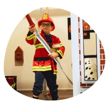 young child in firefighting uniform holding a play hose